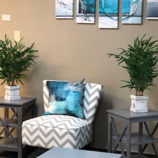 A cozy living room corner featuring a patterned chair, side tables with potted plants, and artwork on the wall.