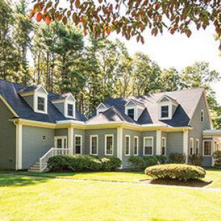 A charming residential house surrounded by a lush lawn and trees, illuminated by daylight.