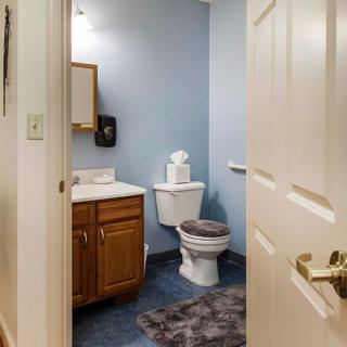A view into a small bathroom with blue walls, featuring a toilet, sink, and mirror.
