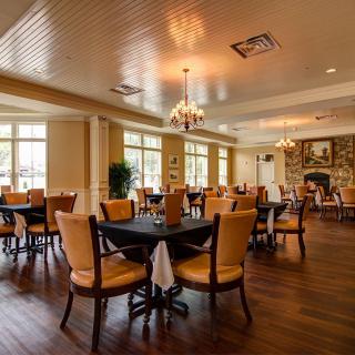 A spacious and elegantly designed restaurant dining area with neatly arranged tables and chairs, warm lighting from chandeliers, and large windows offering ample natural light.