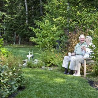 An elderly couple sitting on a bench in a lush garden.