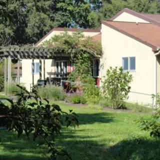 A house with a pergola surrounded by lush greenery and gardens.