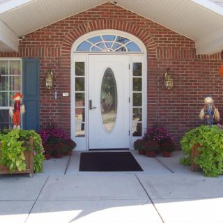 A welcoming entrance with a white, oval-glass front door set in a brick building, flanked by potted plants and outdoor decorations.