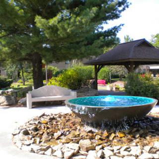 A serene park scene featuring a decorative fountain surrounded by rocks and greenery.