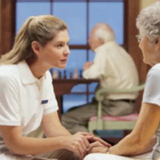 A caregiver converses with an elderly woman in a nursing home.
