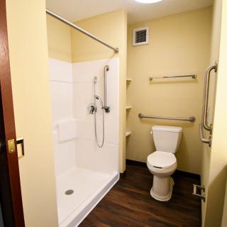 An accessible bathroom featuring a shower with handrails and a toilet.