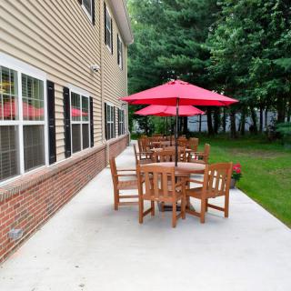 A patio with a wooden table and chairs set under a red umbrella next to a building.
