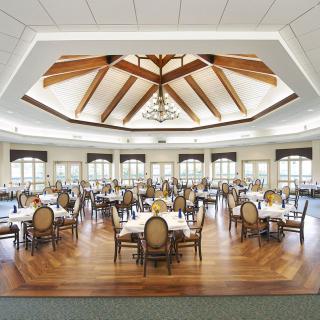 An elegant dining room with wooden floors, set tables, and a unique ceiling design.
