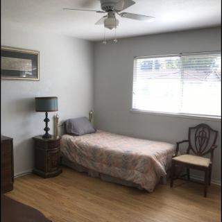 A simple bedroom with a single bed, chair, and lamp near a window.