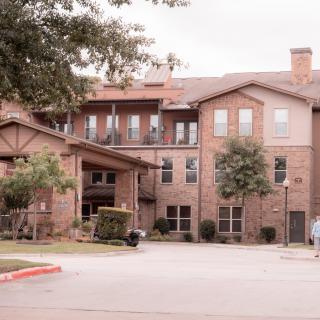 A large residential brick building with multiple stories and surrounding greenery.