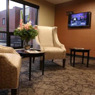A cozy waiting room with comfortable chairs, a small table with flowers, and a television on the wall.