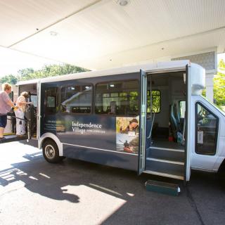 A small shuttle bus picking up passengers at a station during the day.
