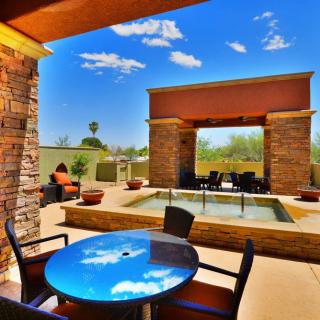 A sunny outdoor patio with a seating area and a fireplace, surrounded by a scenic landscape.
