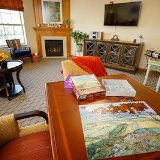 A cozy living room with a puzzle in progress on the table, a fireplace, and a television mounted on the wall.