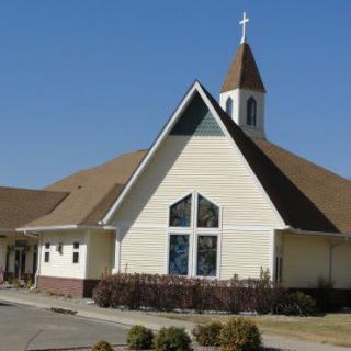 A church building with a prominent cross on the steeple against a clear blue sky.
