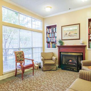 A cozy living room with a fireplace, armchairs, and a bookshelf under large windows.