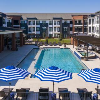 A modern residential complex with a central swimming pool and blue-striped umbrellas.