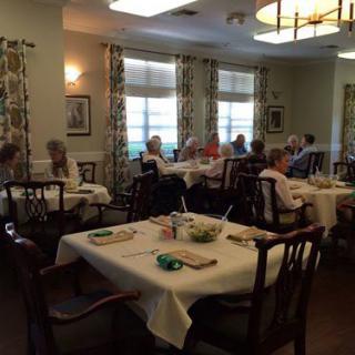 A dining room with several tables set for a meal, occupied by seniors.