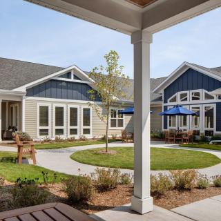 A view of a residential courtyard with blue and beige houses, surrounded by neatly landscaped gardens.