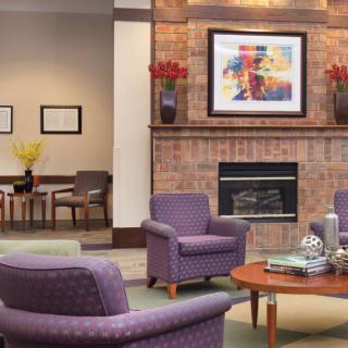 A cozy living room with purple chairs, a fireplace, and colorful artwork above the mantel.