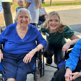 A joyful moment shared between an elderly woman and her caregiver smiles in the sunshine.