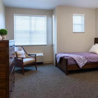A neatly arranged bedroom with a bed, chair, dresser, and windows.