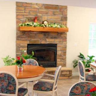 A cozy living room with a stone fireplace and a wooden mantel, adorned with greenery and flowers. Surrounding the round table are chairs with patterned cushions, creating a comfortable and inviting atmosphere.
