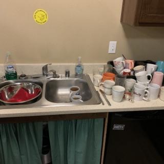 A cluttered kitchen sink with a pile of dirty dishes and mugs on the countertop.