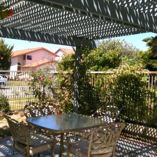 A sunny patio with a pergola casting shadows on a table and chairs.