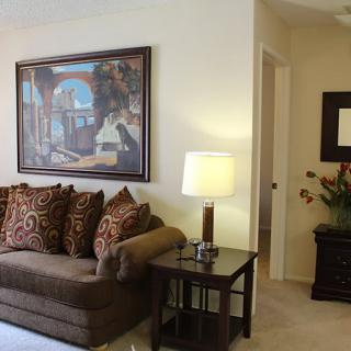 A cozy living room with a brown sofa, side table with a lamp, and artwork on the wall.