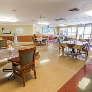 A spacious dining area with multiple tables and chairs, well-lit by natural light from large windows.
