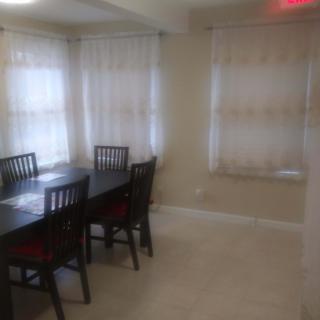 A dining room with a dark wooden table and chairs near windows with sheer curtains.