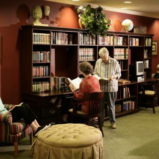 A cozy library setting with several people reading near a large bookshelf.