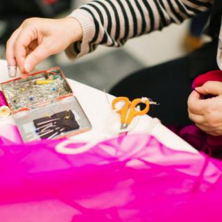A person is engaged in sewing, surrounded by colorful fabric and tools.