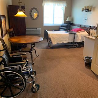 A spacious room equipped with a bed, wheelchair, and a small table, designed for comfort and accessibility.