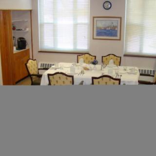 A dining room with a set table, decorated with chairs, artwork on the wall, and a clock.