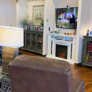 A cozy living room featuring a comfortable chair, a TV mounted on the wall, and an electric fireplace.