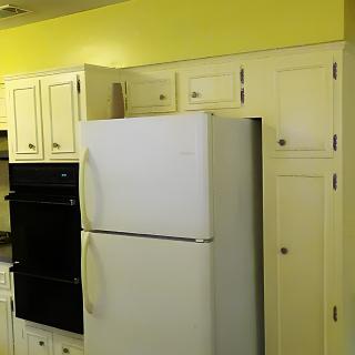 A kitchen with yellow walls, featuring a white refrigerator and cream-colored cabinets.