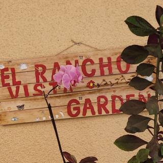 A rustic garden sign with a pink flower in the foreground.
