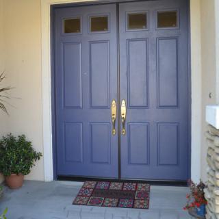 A pair of blue double doors with golden handles, accompanied by a doormat and potted plants.