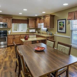A warm and inviting kitchen with wooden cabinets and dining area, featuring modern appliances and a hardwood floor.