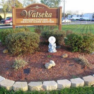 Welcome sign for Watsheka surrounded by greenery and decorative stones.