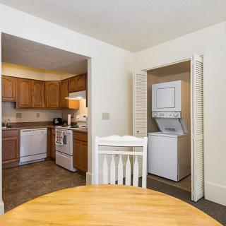 A cozy interior view featuring a kitchen area with wooden cabinets and a nearby laundry nook containing a stacked washer and dryer.