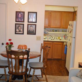 Cozy dining area leading into a kitchen, featuring a round wooden table adorned with flowers.