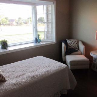 A cozy bedroom with a large window letting in natural light, featuring a bed and an armchair.