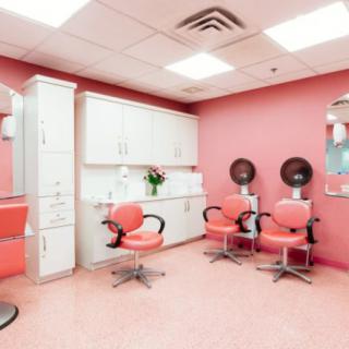 A brightly lit salon with pink walls, featuring styling chairs and hair dryers.