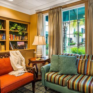 A cozy living room with vibrant sofas and a bookshelf, illuminated by natural light through the window.