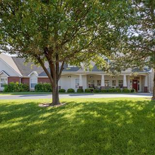 A picturesque suburban house with a well-maintained lawn and large trees casting shadows in the sunlight.