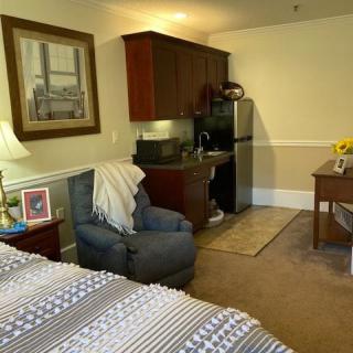 Cozy bedroom with a small kitchenette, featuring an armchair and a desk.