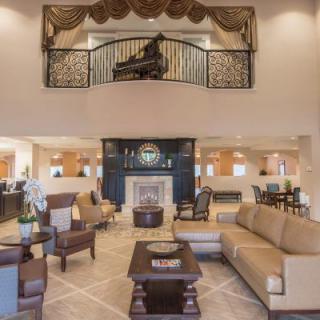 A luxurious living room with elegant furniture, a grand piano on the mezzanine, and a central fireplace.